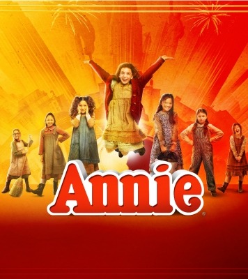 The word Annie with seven girls standing in a V formation and the one in the middle jumping throwing her hands in the air