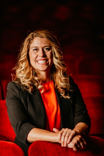 Woman with dirty blonde hair with a black blazer and red blouse